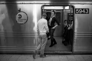 Confident man approaches a smiling woman on a New York City subway train
