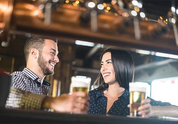 Young couple at beginnings of love story - Pretty woman drinking beer with handsome man at pub - Relationship lovers concept with drunk boyfriend and girlfriend together at brewery - Warm retro filter